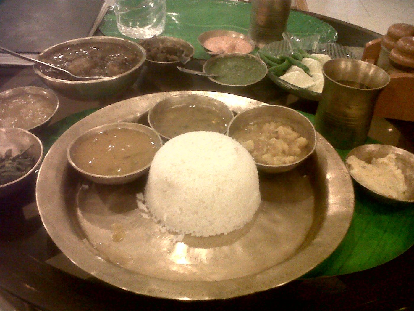 An Assamese thali with rice, dal, fish curry and small bowls of sides on a bell-metal plate