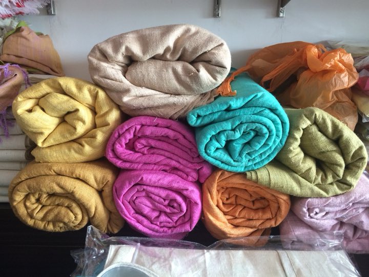 Rolls of eri silk cloth in yellow, pink, teal, orange and cream stacked on a shelf