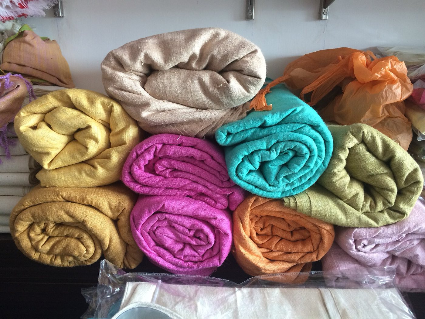 Rolls of eri silk cloth in yellow, pink, teal, orange and cream stacked on a shelf